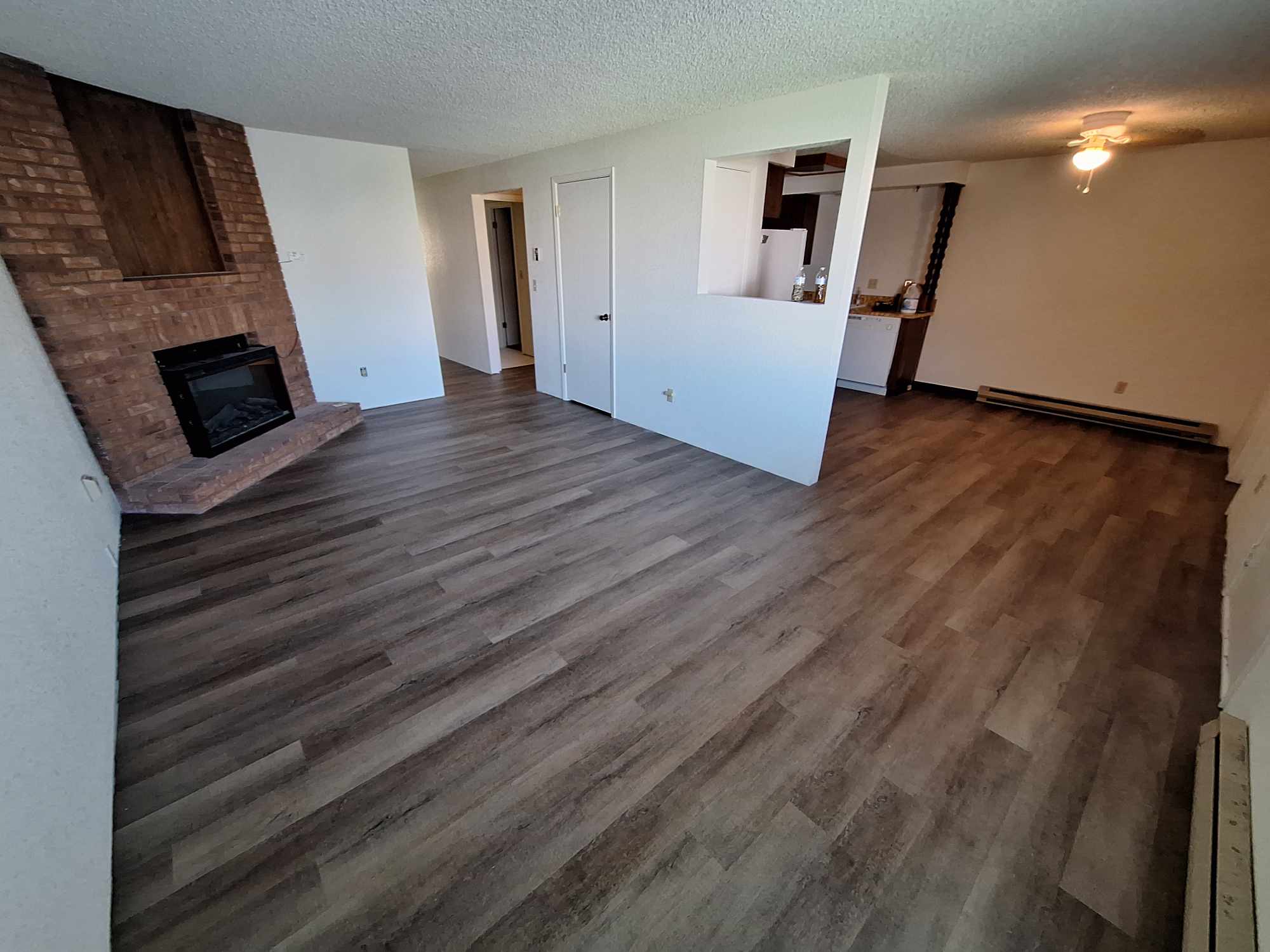 Large living room with dark wood grain vinyl flooring and red brick fireplace