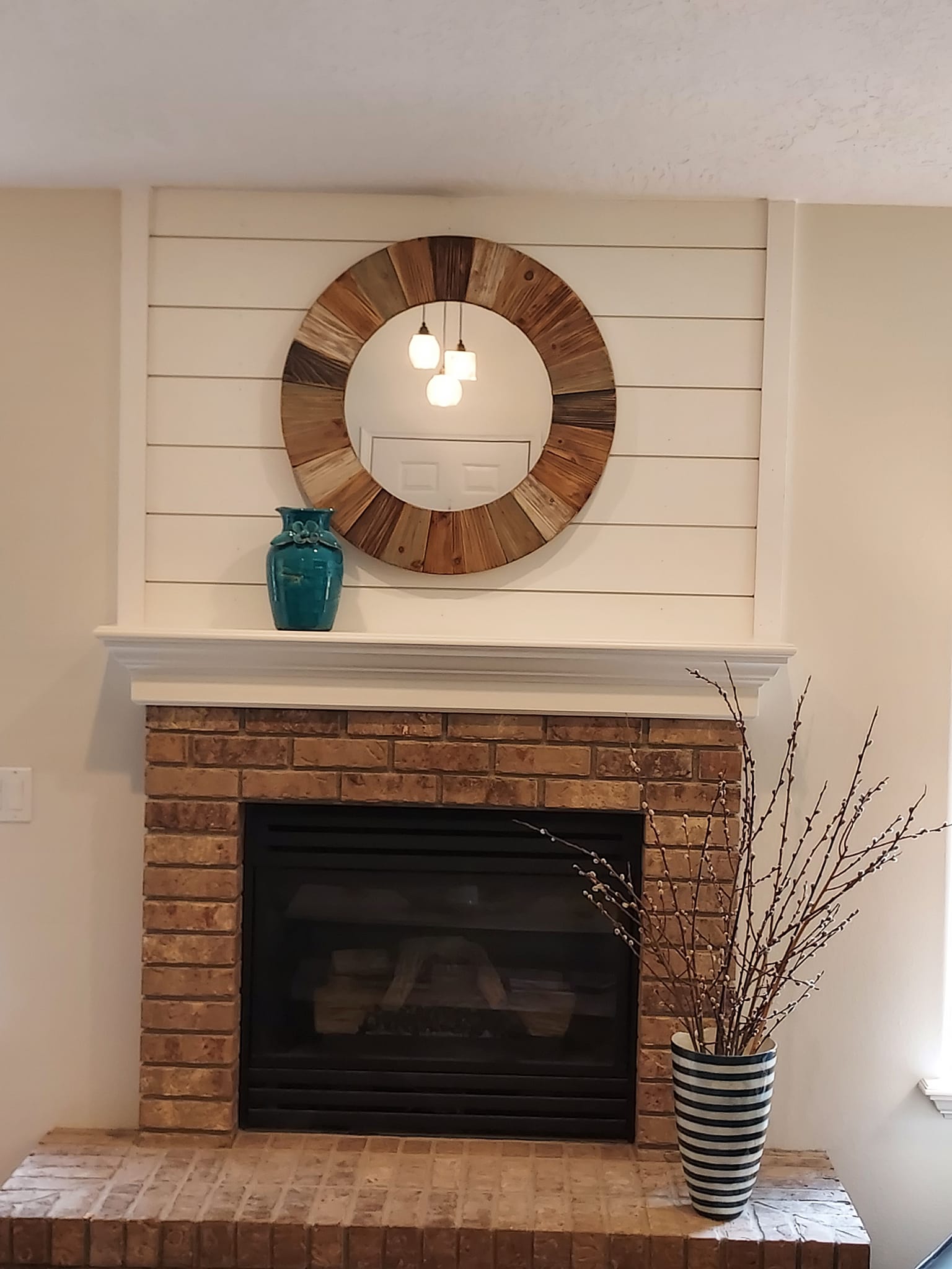 Red brick fireplace with round mirror and white wood planks above