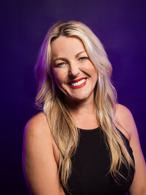 April, founder and director of Dancing for Joy, smiling warmly with long blonde hair against a purple studio background