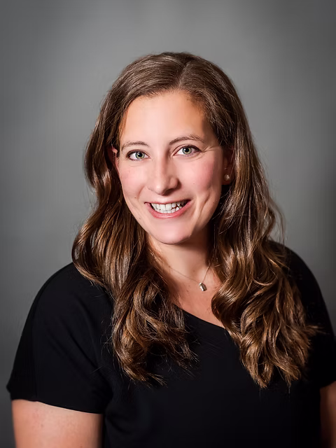 Hannah, instructor, with long wavy brown hair and a warm, approachable smile against a gray background