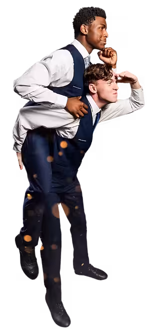 Two male dancers in dress shirts and vests strike a playful partnered pose, one riding on the other's back while both look off into the distance.